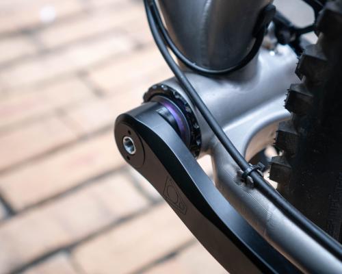Non-drive side crank arm mounted to a mountain bike, a purple anodized spacer peeks out.